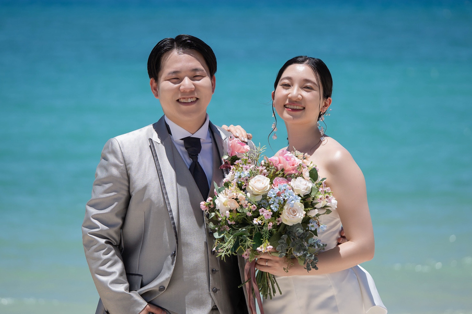 青い海を背景に笑顔で並ぶ新郎新婦