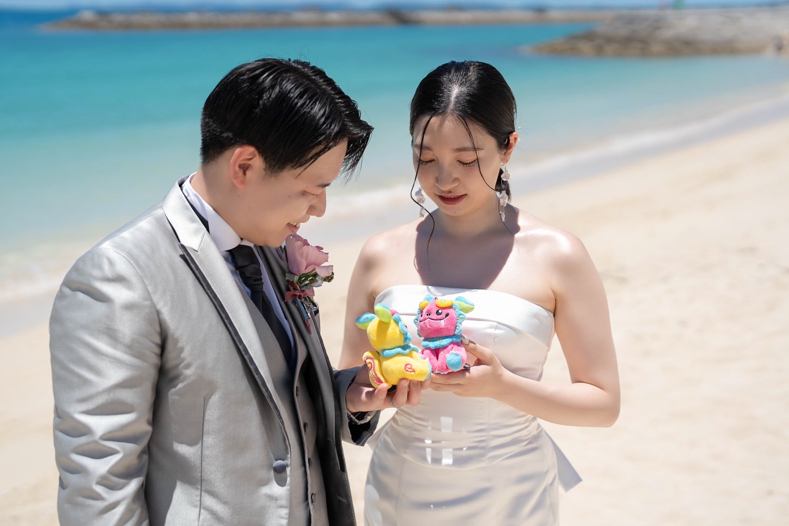 沖縄のぬいぐるみを手に砂浜で見つめる新郎新婦