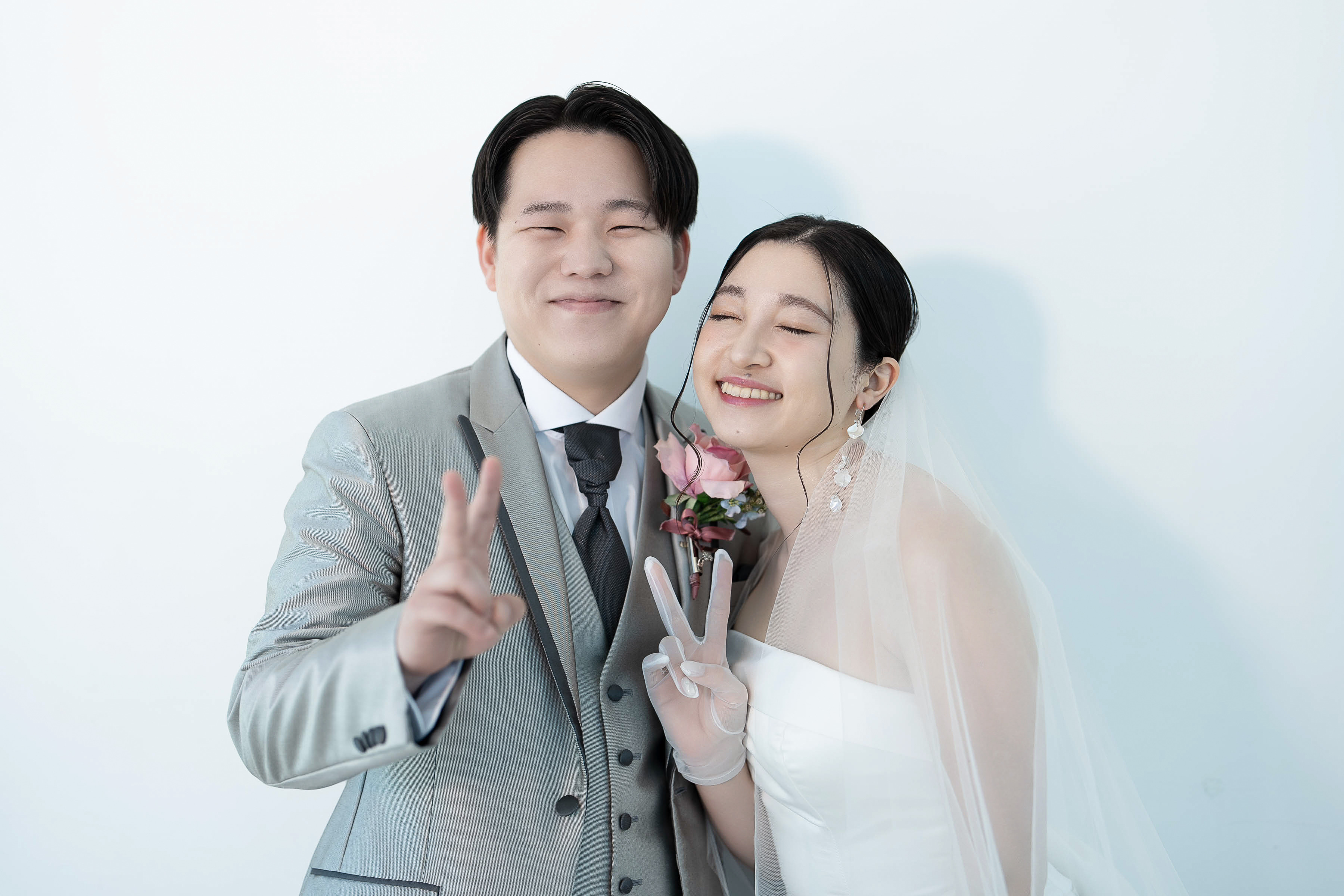 白い壁の前で笑顔のピースサインを見せる新郎新婦